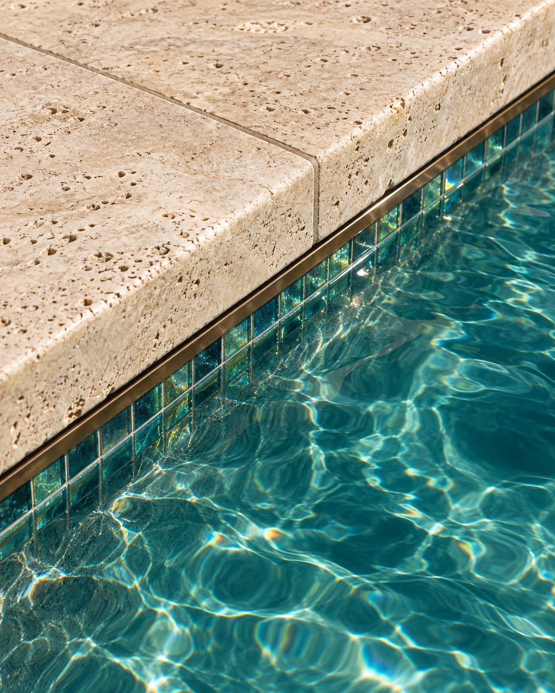 Concept detail of textured travertine coping, glass mosaic tile and sunlit turquoise water
